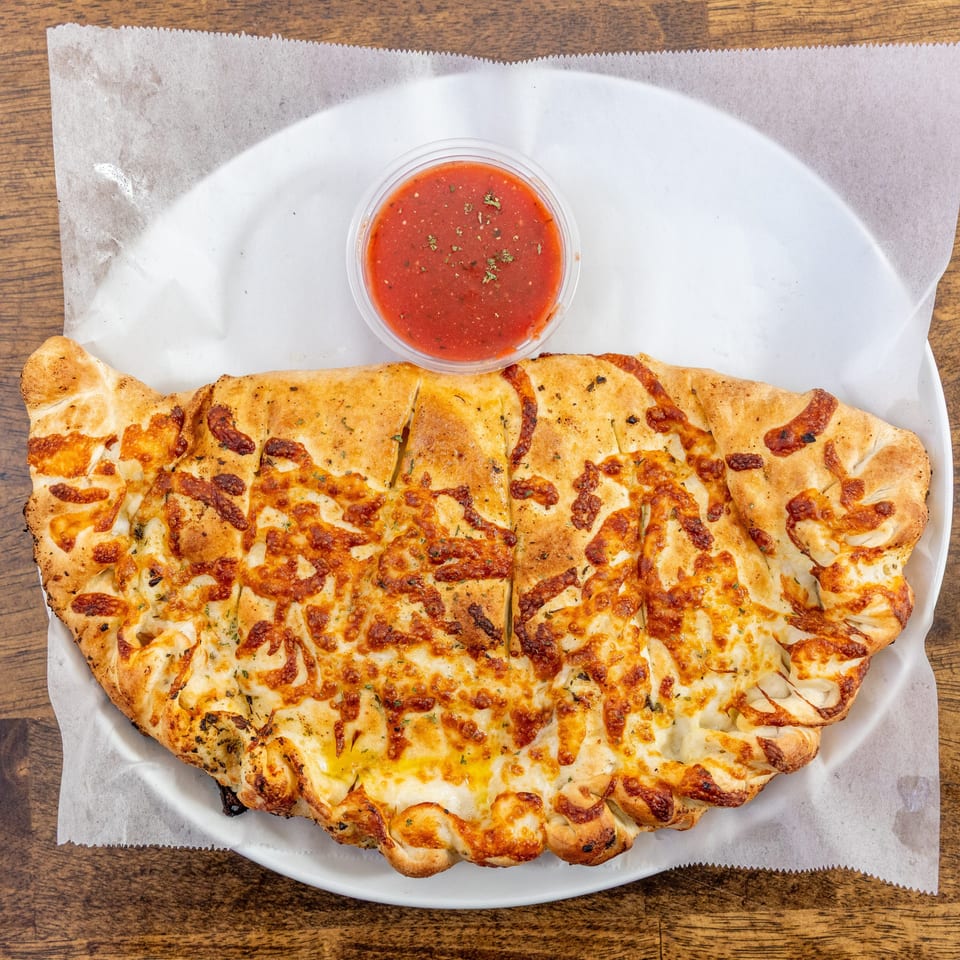 A golden-brown calzone, sliced into pieces, with melted cheese and a side of marinara sauce.