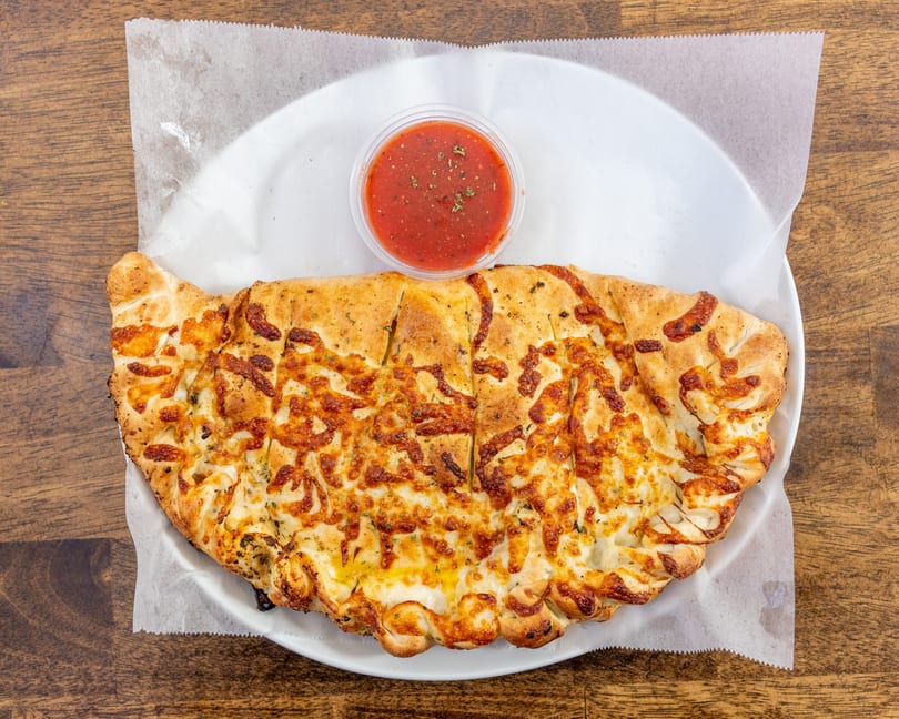A golden-brown calzone, sliced into pieces, with melted cheese and a side of marinara sauce.