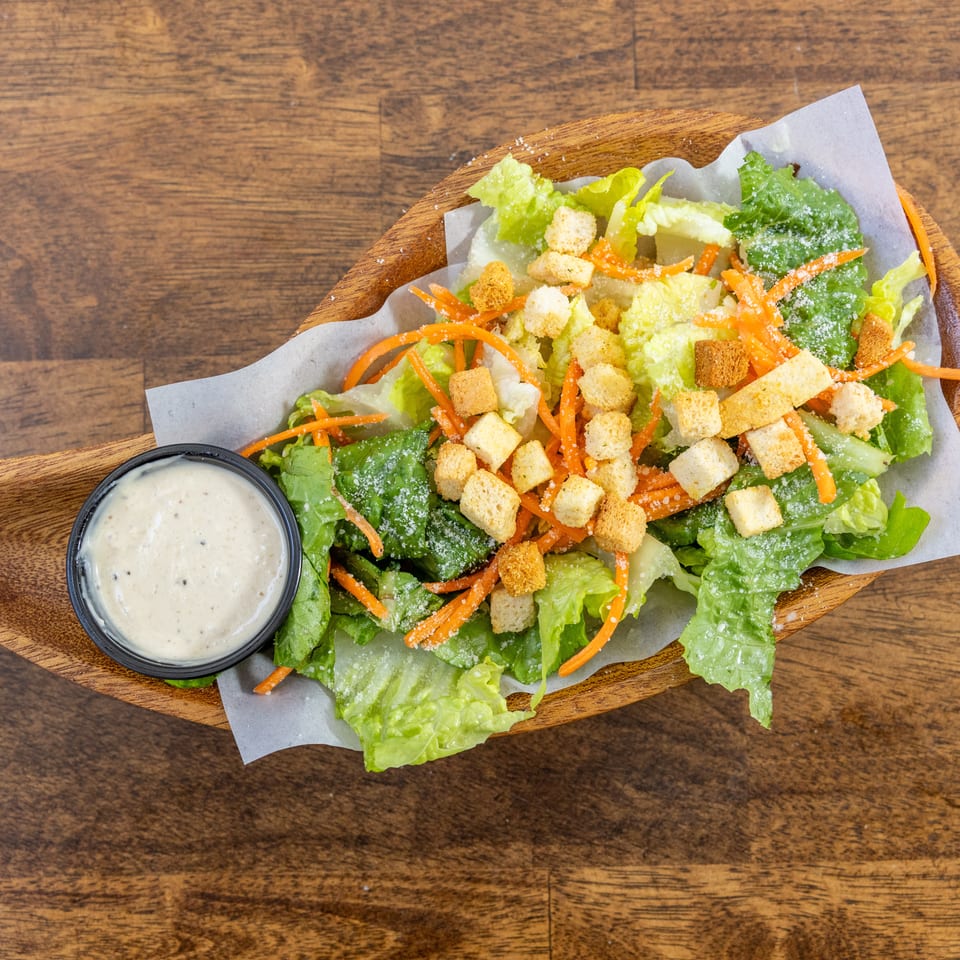 Caesar salad with lettuce, shredded carrots, croutons, parmesan cheese, and a side of dressing.