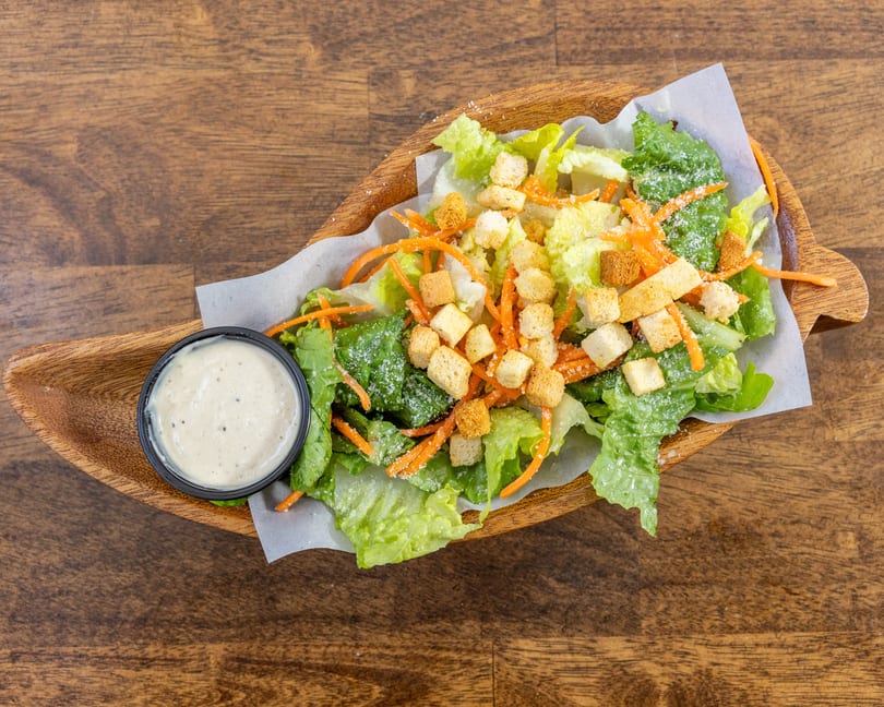 Caesar salad with lettuce, shredded carrots, croutons, parmesan cheese, and a side of dressing.