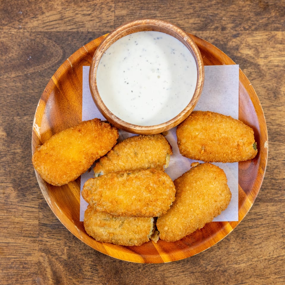 Golden-brown fried jalapeño poppers and a bowl of creamy ranch dip on a wooden plate.