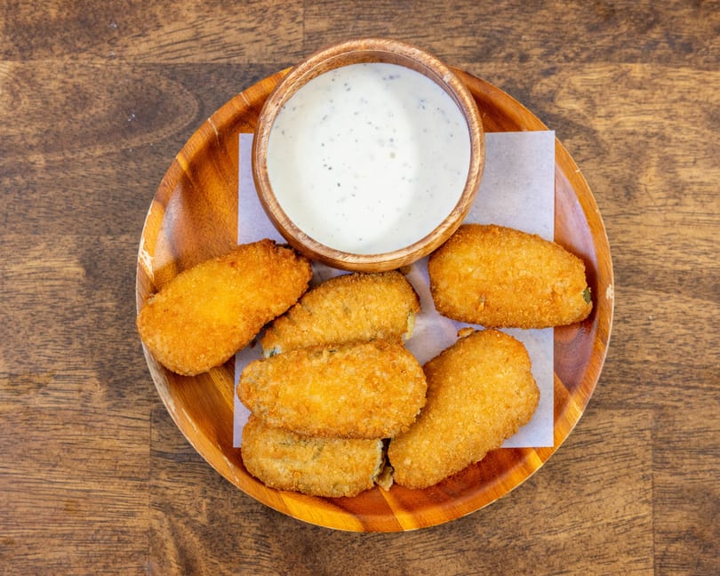 Golden-brown fried jalapeño poppers and a bowl of creamy ranch dip on a wooden plate.