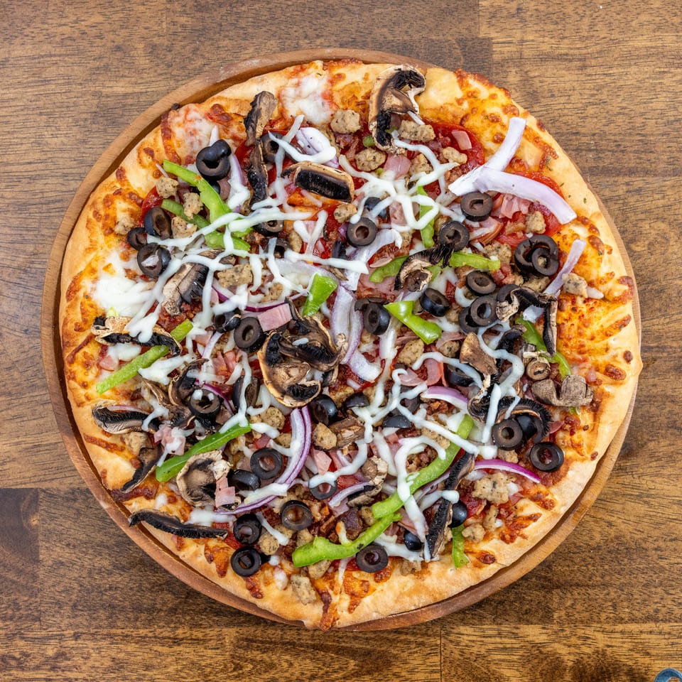 Overhead view of a supreme pizza with olives, mushrooms, peppers, onions, and sausage on a wooden board.