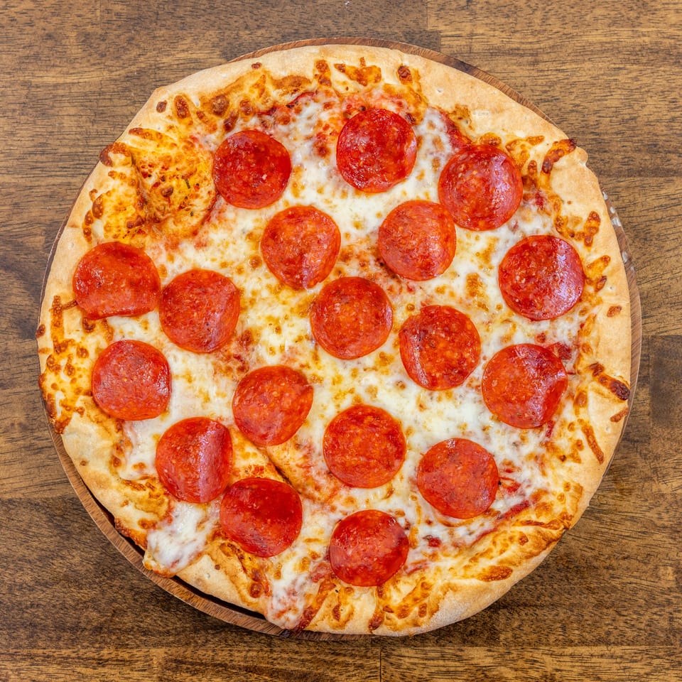 A whole pepperoni pizza with melted cheese and a golden crust, on a wooden table.