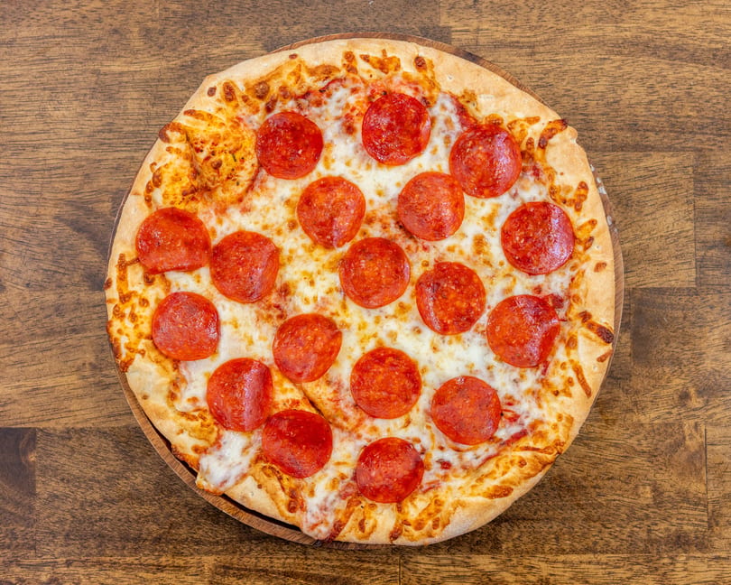 A whole pepperoni pizza with melted cheese and a golden crust, on a wooden table.