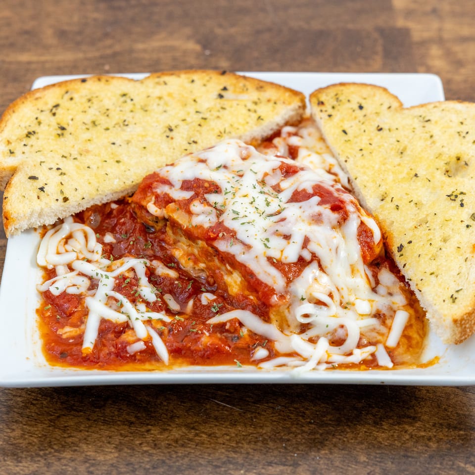 A serving of lasagna with melted cheese and tomato sauce, flanked by two slices of garlic bread.