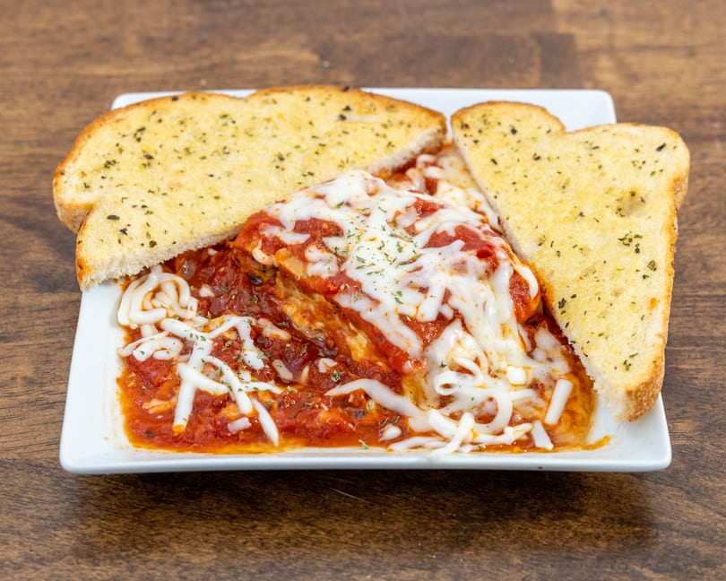 A serving of lasagna with melted cheese and tomato sauce, flanked by two slices of garlic bread.