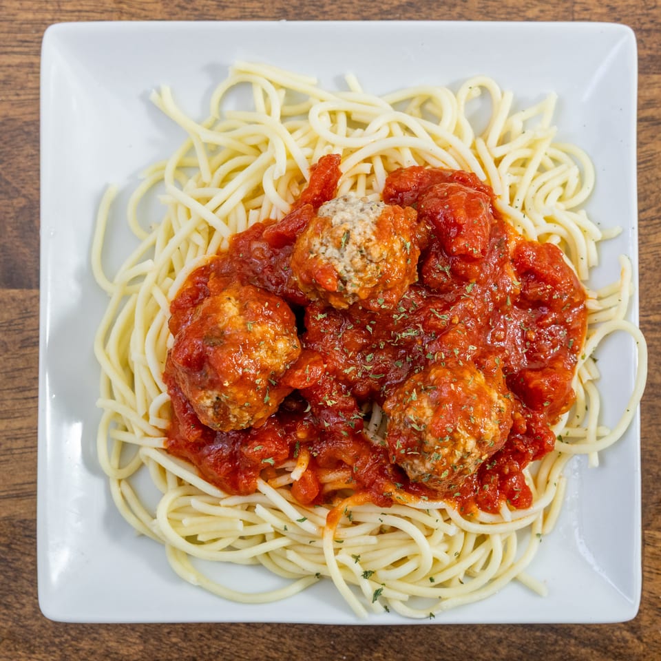 Spaghetti with meatballs and red sauce, garnished with herbs, on a white square plate.