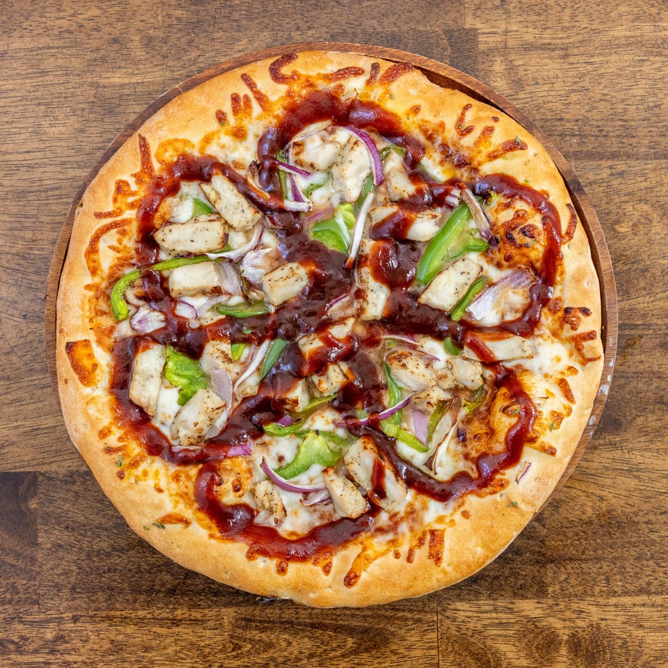 BBQ chicken pizza with green peppers and red onions on a wooden board.