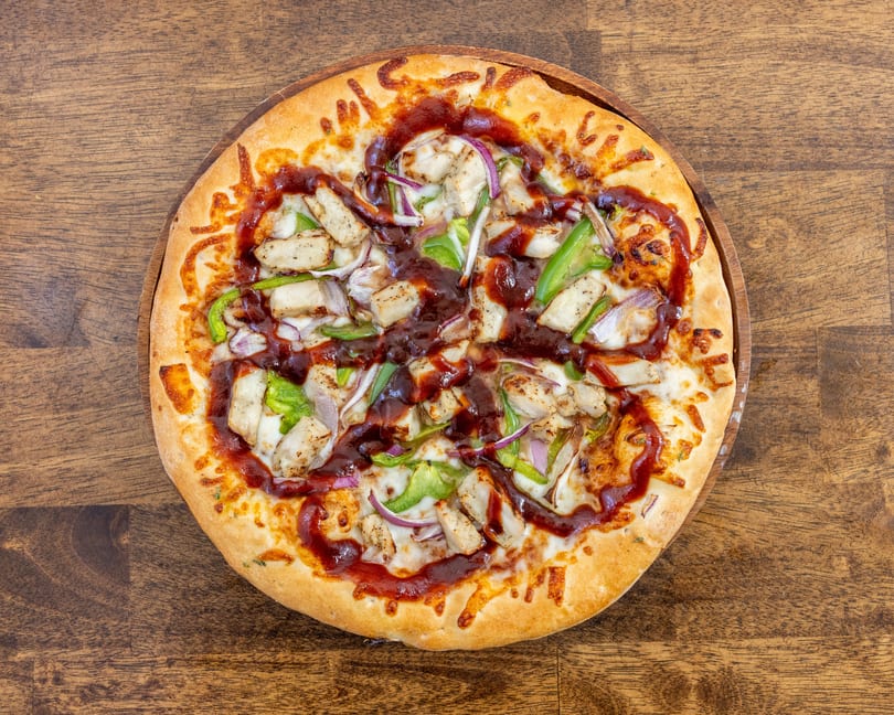 BBQ chicken pizza with green peppers and red onions on a wooden board.